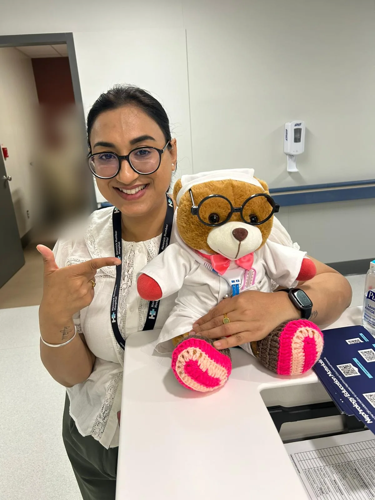 Jasraj Kaur, RN, smiling beside a nurse teddy bear at a nephrology education desk