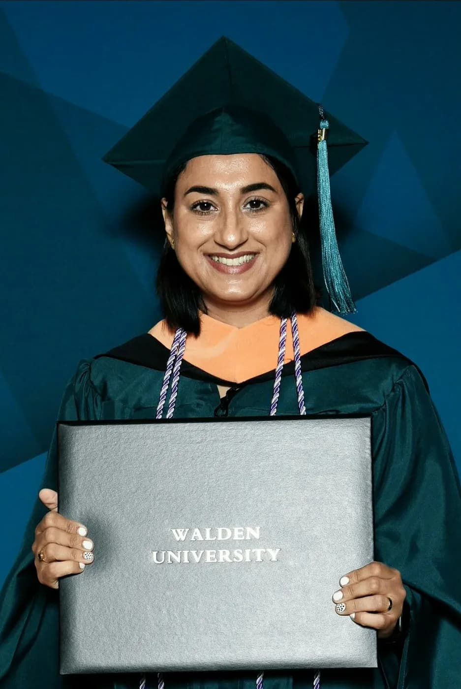 Jasraj in graduation cap and gown holding her Walden University diploma